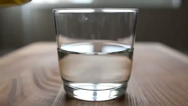 A drop of golden oil falling into a glass of water and floating as a round bead without mixing